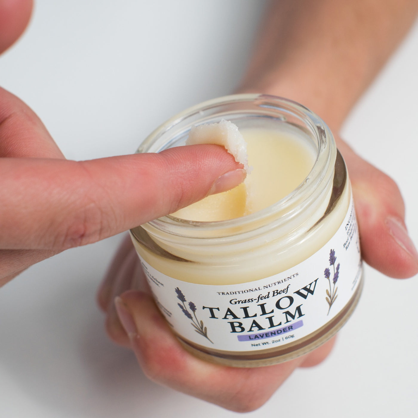 A small scoop of Lavender balm on a fingertip above the open jar